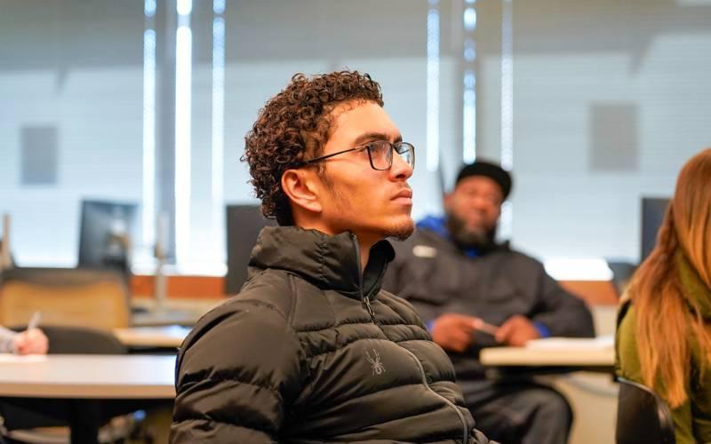 A student wearing a black jacket sits attentively in class